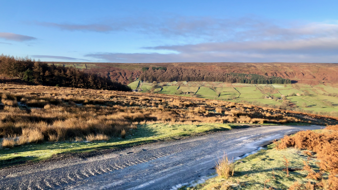 Early morning view of Bransdale from the top of Shaw Ridge. Blue sky and brilliant sunshine. In the foreground an ice covered road portrays the temperature.
