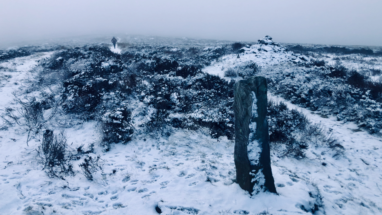 Snowy scene of a standing stone with a runner in the distance.