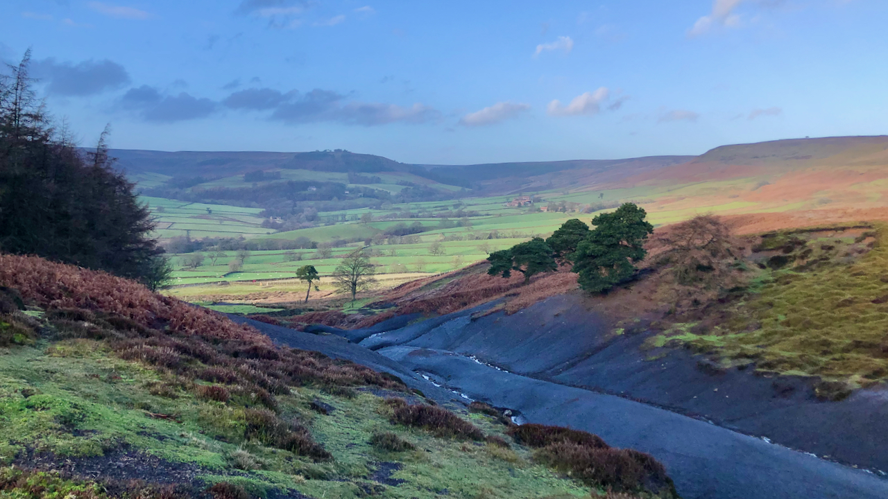 A view of Bransdale in the North York Moors. Blue sky and sunshine. In the foreground a gulley with exposed sides of lias shales.