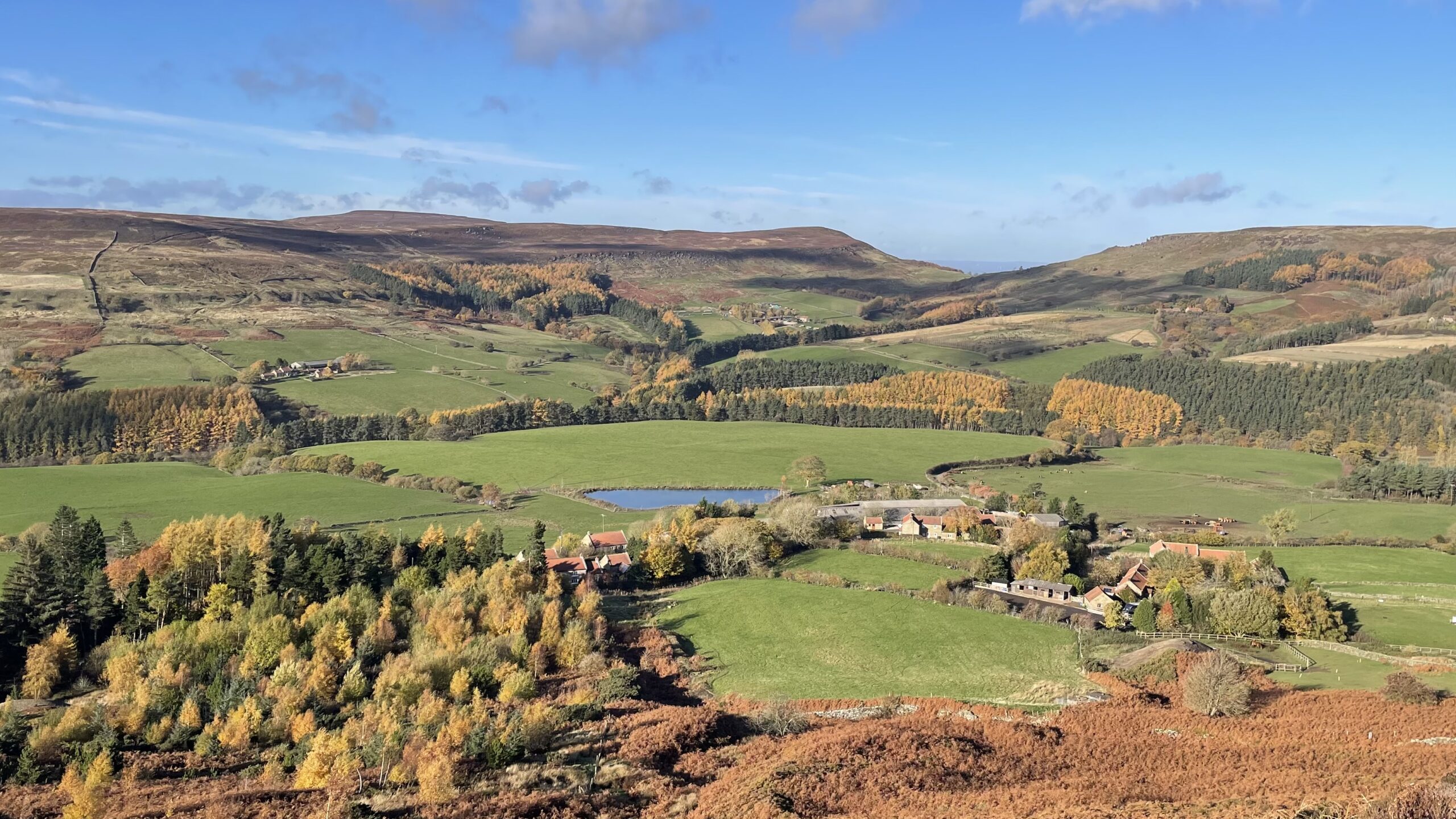 A view of Bilsdale and the hamlet of Urra in autumn, with the Cleveland Hills in the background under a blue sky.