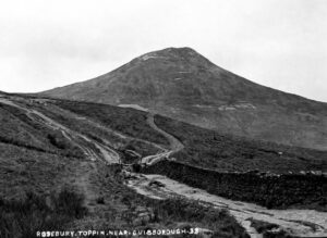 Black and white photograph of Roseberry Topping, a cone-shaped hill near Guisborough, seen from the north-east. A rough cart track leads towards the summit, running alongside a dry-stone wall with a wooden gate. The slopes are bare of trees, covered only in low grass and heather. Caption reads "Rosebury Toppin near Guisborough".