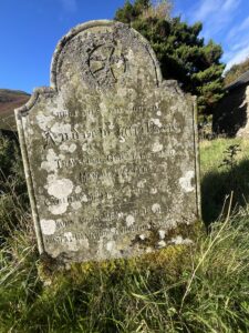 Close-up of Andrew Wilson's lichen-covered gravestone showing the engraved inscription and a carved Celtic cross at the top.